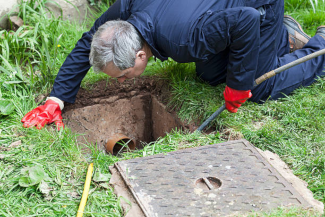 Un plombier professionnel en uniforme de travail, portant une ceinture à outils et travaillant sur des tuyaux sous un évier. Il utilise une clé pour resserrer un raccord, entouré de divers outils de plomberie comme des pinces et un ruban d'étanchéité.